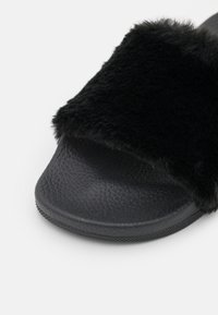 Sandale slide noire avec semelle texturée et large bride en fausse fourrure noire douce sur le dessus.