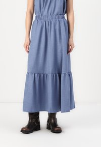 Blå chambray maxi-skjørt med elastisk midjebånd, med lagdelt hem og glatt tekstur, kombinert med brune skinn ankelstøvler.