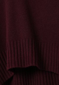 Gros plan d’un tissu tricoté bordeaux foncé plié avec une texture côtelée le long du bord.