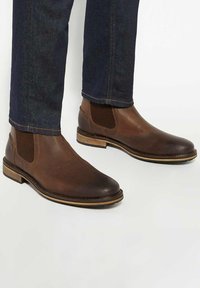 Brown leather Chelsea boots with elastic side panels, a rounded toe, and a contrasting brown sole. Textured surface and classic design.
