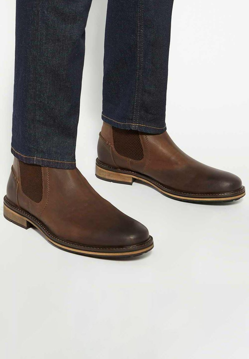 Brown leather Chelsea boots with elastic side panels, a rounded toe, and a contrasting brown sole. Textured surface and classic design.