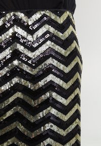 Jupe noire avec un motif en zigzag créé avec des sequins dorés et noirs, mettant en valeur la texture et les surfaces réfléchissantes des embellissements.