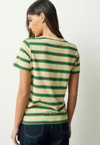 Beež triiksärk roheliste ja pruunide horisontaalsete triipudega, lühikeste varrukatega ja ümar kaelusega. Materjal tundub pehme ja kerge.