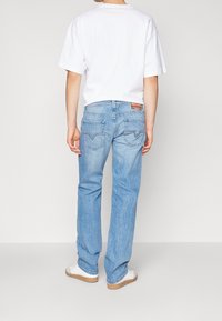 Ljusblå denimjeans med rak passform, med distinkta bakfickor och en Levi's-logotyp på midjebandet. Vit t-shirt som bärs.