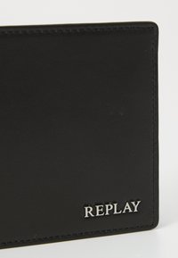Sort læderpunge med en glat overflade, stikninger langs kanterne og et sølvfarvet "REPLAY"-logo i nederste højre hjørne.