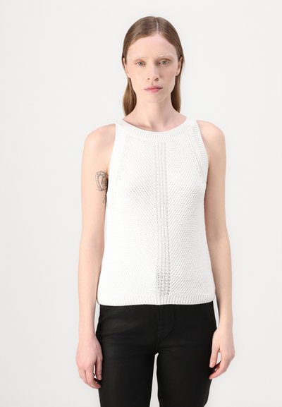 Débardeur sans manches en tricot blanc avec un col côtelé et un motif texturé, associé à un pantalon noir ajusté. Tissu lisse et lignes épurées.