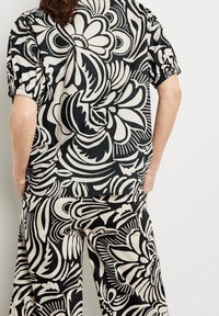 Haut et pantalon à motifs noirs et crème avec tissu fluide. Présente des motifs floraux audacieux et abstraits, des manches courtes bouffantes et une coupe décontractée.