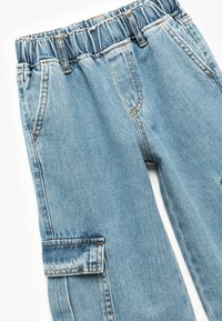 Lichtblauwe denim broek met een elastische tailleband, vijf zakken en taps toelopende benen. Beschikt over zichtbare stiksels in oranje.