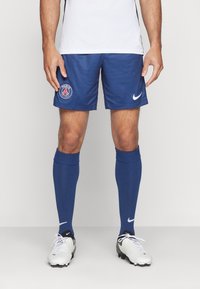 Marinblå fotbollsshorts med logotyp, i kombination med matchande knästrumpor. Vita skor med svarta accenter och snören.