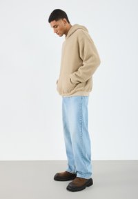 Beige fleece hettegenser med kengurulomme, kombinert med lyseblå jeans og brune robuste støvler. Glatt tekstur, avslappet passform.