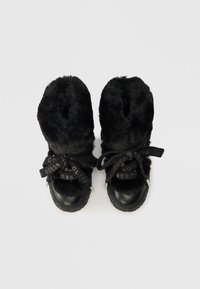 Black faux fur boots with shiny black leather accents, featuring thick black laces with "GUESS" logo and round rubber soles.