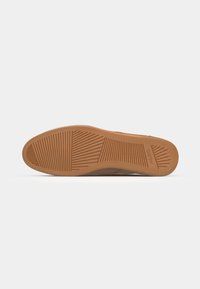 Suela de un zapato con un diseño de goma texturizada y de color marrón claro. Presenta surcos y patrones para aumentar la tracción.