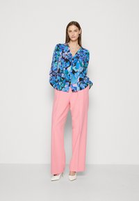 Blusa floreale nei toni del blu, verde e rosa, abbinata a pantaloni a gamba larga rosa e décolleté bianchi a punta. Tessuto morbido con un fit largo.