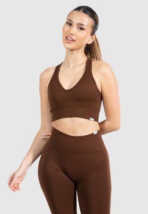 Bruine geribbelde sportbeha met een diepe V-hals, uitsnijdingen en bijpassende hoge taille leggings. Gladde textuur, aansluitende silhouet.
