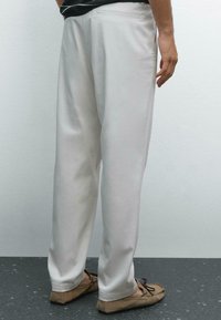Pantaloni bianchi su misura con vestibilità dritta, tessuto liscio e dettaglio della tasca posteriore. Abbinati a mocassini color marrone chiaro.