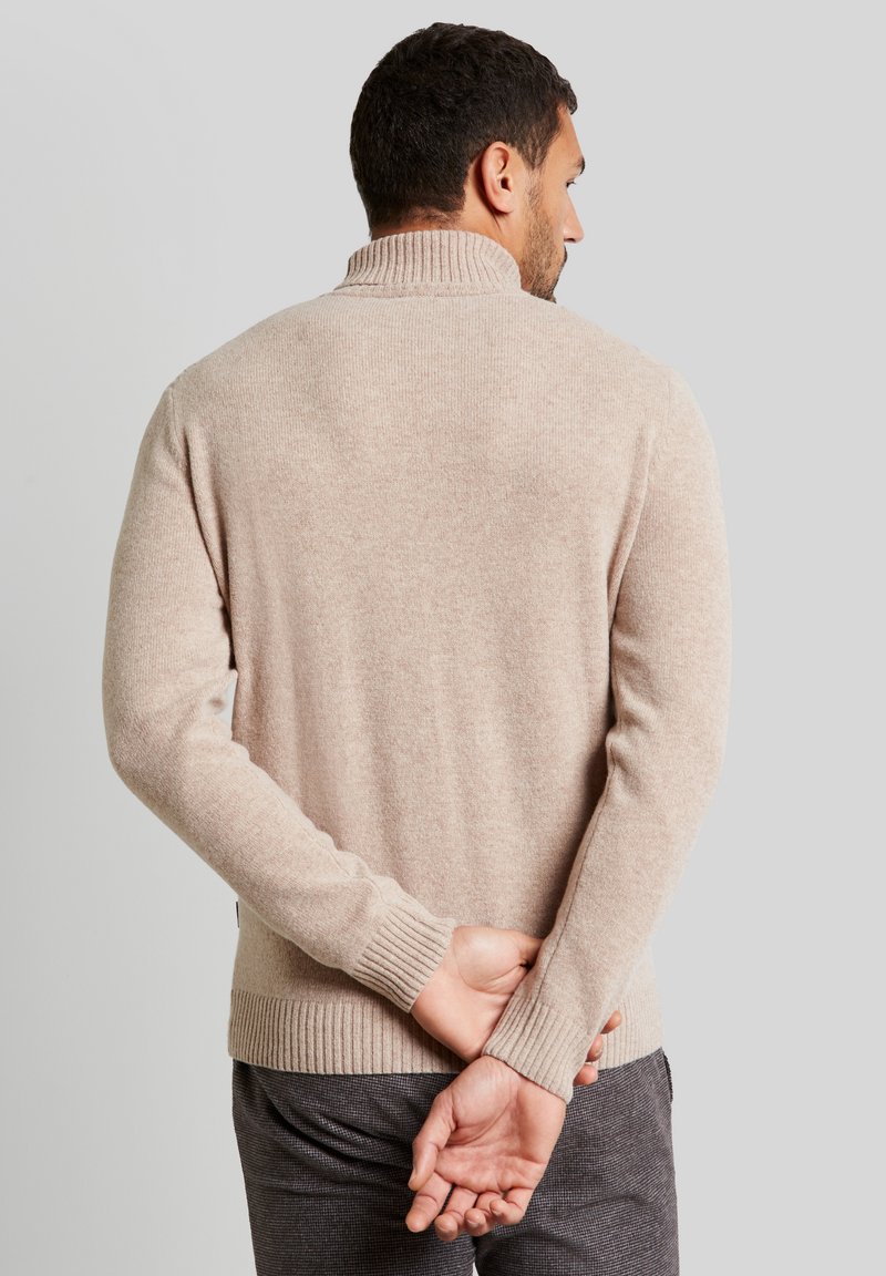 Maglione beige a maglia con colletto alto, polsini e orlo a costine. Il tessuto appare morbido e leggermente strutturato, progettato per una vestibilità aderente.