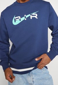 Blå sweatshirt med stor "AIR"-logotyp i vitt och aqua. Figursydda muddar och fåll med randig detalj längst ner. Tillverkad i bomull.