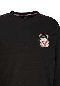 Zwarte sweatshirt met een geborduurd berenontwerp in een pet en de tekst "APRES SKI" in het rood. De stof lijkt glad en zacht.
