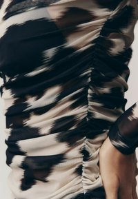 Ruched dress with black and beige abstract pattern, featuring a sheer texture and fitted silhouette, emphasizing lines and curves.