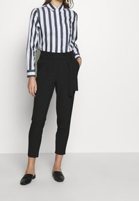 Randig långärmad skjorta i marinblått och vitt, tillsammans med högmidjade svarta byxor med knytdetalj fram och smalnade ben. Svarta slip-on skor.