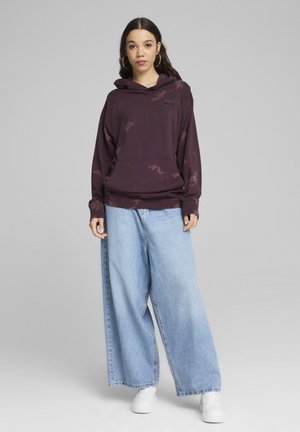 Felpa con cappuccio viola tie-dye, dotata di tasca a marsupio e patch con logo, abbinata a jeans boyfriend in denim azzurro chiaro e sneakers bianche.