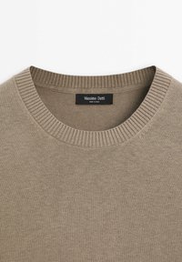 Beige gestrickter Pullover mit einem gerippten, runden Halsausschnitt. Verfügt über eine glatte Textur, leichtes Material und ein schwarzes Etikett mit Markeninformationen.