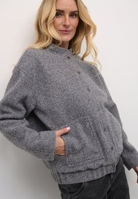 Giacca in pile grigia con colletto alto, dotata di chiusura con bottoni e tasche laterali. Tessuto strutturato e design con vestibilità rilassata.