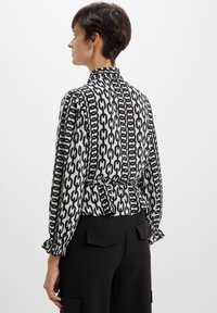 Blusa a righe bianche e nere con motivo a catena, colletto alto, maniche a sbuffo e polsini arricciati, abbinata a pantaloni neri.