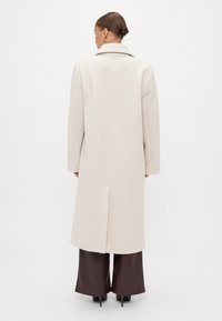 Κρέμα παλτό με υφασμάτινη υφή, με κοφτό γιακά και ευθύ κόψιμο. Διαθέτει πίσω άνοιγμα για ευκολία στην κίνηση.