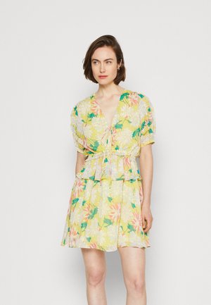 Φλοράλ φόρεμα με έντονο κίτρινο φόντο, που διαθέτει φουσκωτά μανίκια, ζώνη που τονίζει τη μέση και φούστα με επίπεδα. Τα σχέδια περιλαμβάνουν μεγάλα λουλούδια σε ροζ και πράσινο χρώμα.