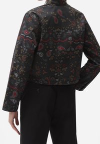 Svart kort jacka med ett paisleymönster i röd, gul och vit. Tyget har en slät textur med knappdetaljer och en hög krage.