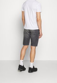Pantalones cortos de mezclilla gris con un acabado ligeramente desvanecido, de longitud por encima de la rodilla, combinados con una camiseta blanca lisa y zapatillas negras, contra un fondo neutro.