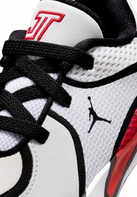 Biało-czarny sneaker z czarnymi sznurowadłami, czerwonymi akcentami, teksturowaną tkaniną i czarnym logo Jumpman po bokach, w okolicy kostki.