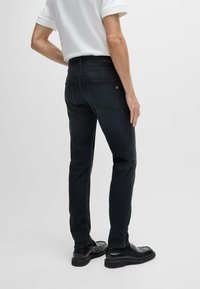 Dark denim jeans with a slim fit, five-pocket design, and a logo patch at the waistband. Smooth texture, straight leg cut, and minimal stitching.