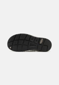 Black rubber shoe sole with textured grip pattern, featuring a pronounced contour arch and a triangular accent near the heel.