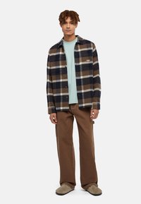 Flannel skjorte i marineblå, brun og cremeplaid; lagdelt over en lys blå T-shirt; parret med brede brune bukser og grå fuzzy slippers.