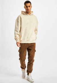 Hoodie crème avec le logo "DEF", associé à un pantalon cargo en velours côtelé marron avec des poches latérales. Des baskets montantes blanches complètent la tenue.
