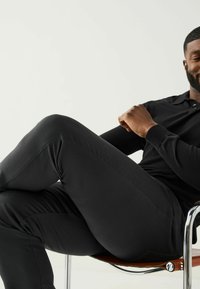 Juoda ilgomis rankovėmis polo marškinėliai derinami su prigludusiomis juodomis kelnėmis, pristatomi sėdint ant chromo ir odos kėdės. Lygi tekstūra.