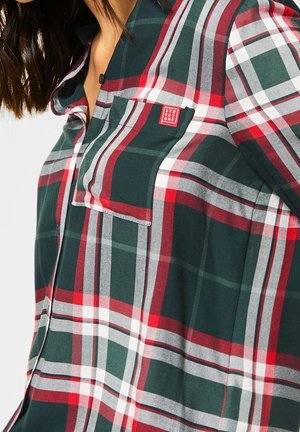 Mujer con una camisa de cuadros en verde, rojo, blanco y negro, con botones y un bolsillo en el pecho etiquetado como "Street One".