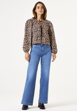 Blouse à imprimé léopard, à manches longues, avec un design court et des accents de boutons noirs, associée à un jean flared taille haute, bleu clair.