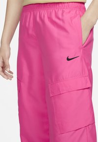 Rosa cargobyxor med elastisk midja, sidofickor och en svart Nike-logotyp på övre vänstra benet. Slät, lätt tyg.