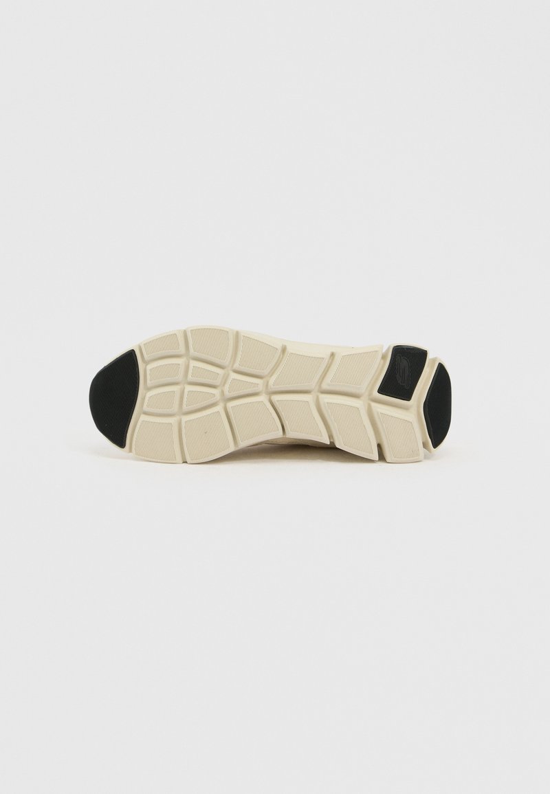 Suela de zapato con un patrón de tracción multidireccional, con una base crema y acentos de goma negra para mayor durabilidad y agarre.