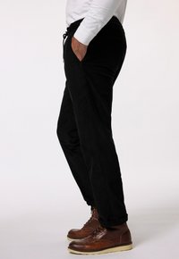 Zwarte corduroy joggers met een elastische tailleband en zijzakken, gecombineerd met bruine veterschoenen met een gestructureerde leren afwerking.