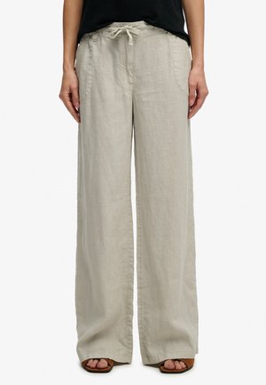 Pantalon large en lin beige avec poches avant et taille à cordon, porté avec un haut noir et des sandales ouvertes marron.