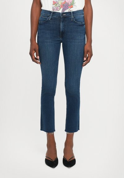 Jeans en denim bleu foncé avec une coupe slim, un ourlet effiloché et un design à cinq poches. Associés à des escarpins noirs à bout pointu.