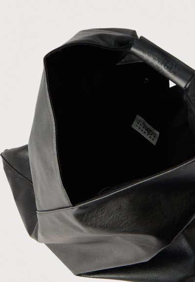 Μαύρη τσάντα ώμου από μαλακό δέρμα με ανοιχτό πάνω μέρος που αποκαλύπτει εσωτερική ετικέτα με κυκλωμένο αριθμό 6 και τυπωμένους αριθμούς σε λευκή ετικέτα.