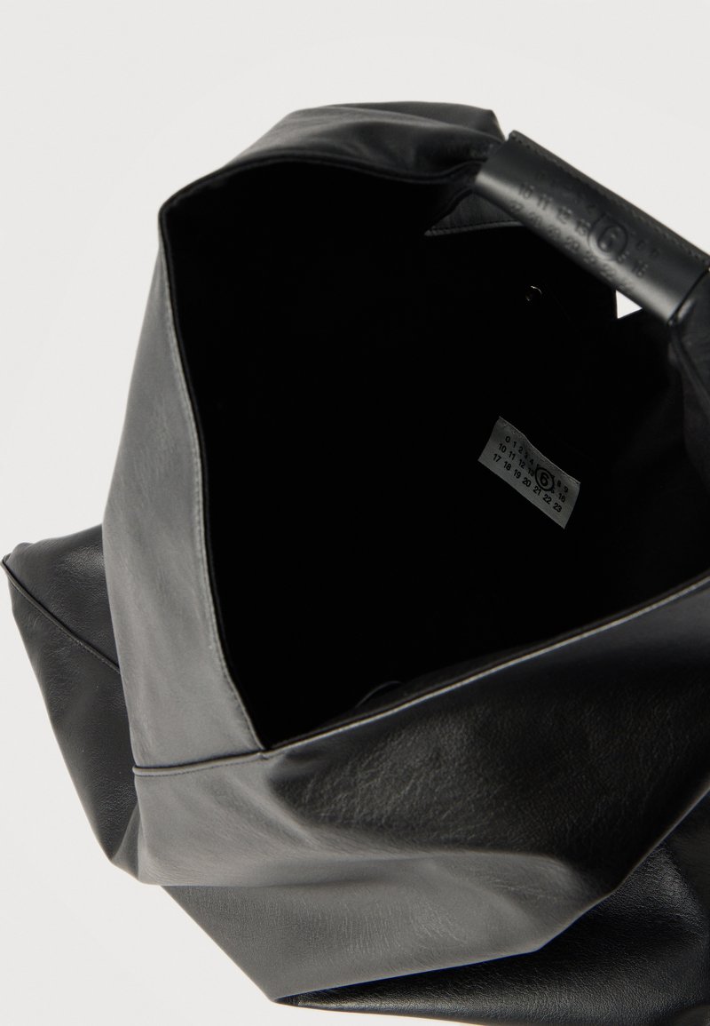 Sac cabas en cuir souple noir avec ouverture supérieure montrant une étiquette intérieure affichant un numéro 6 cerclé et des chiffres imprimés sur une étiquette blanche.