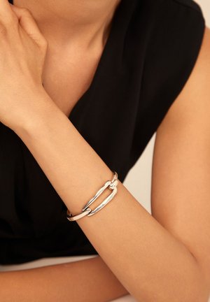 Pulsera de plata con eslabones ovalados entrelazados y un acabado suave, llevada en una muñeca desnuda sobre un fondo de tela oscura.