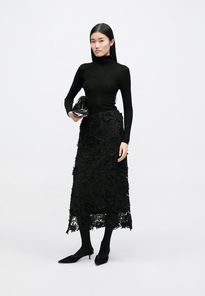 Un pulover negru cu guler înalt texturat, fustă midi din dantelă florală, asortat cu o geantă de mână neagră din lac și pantofi cu vârful ascuțit. Textură netedă și detalii stratificate.