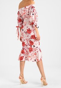 Sukienka bez ramiączek w kwiaty w jasnoróżowym kolorze, z czerwonymi kwiatami, bufiastymi rękawami z wiązaniami i rozkloszowanym dołem. Noszona z cielistymi sandałami na wysokim obcasie.